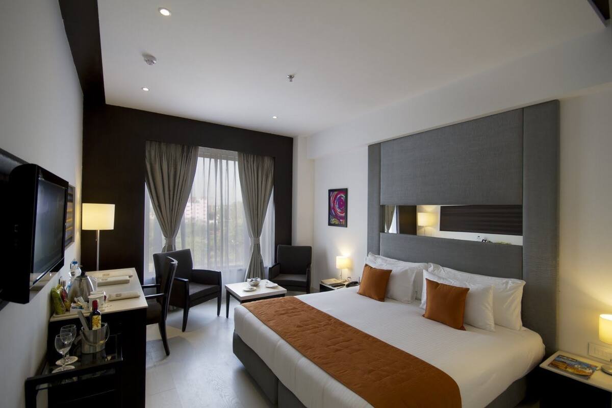 A hotel room with a large bed, a desk with a TV, a chair, and a window with curtains.