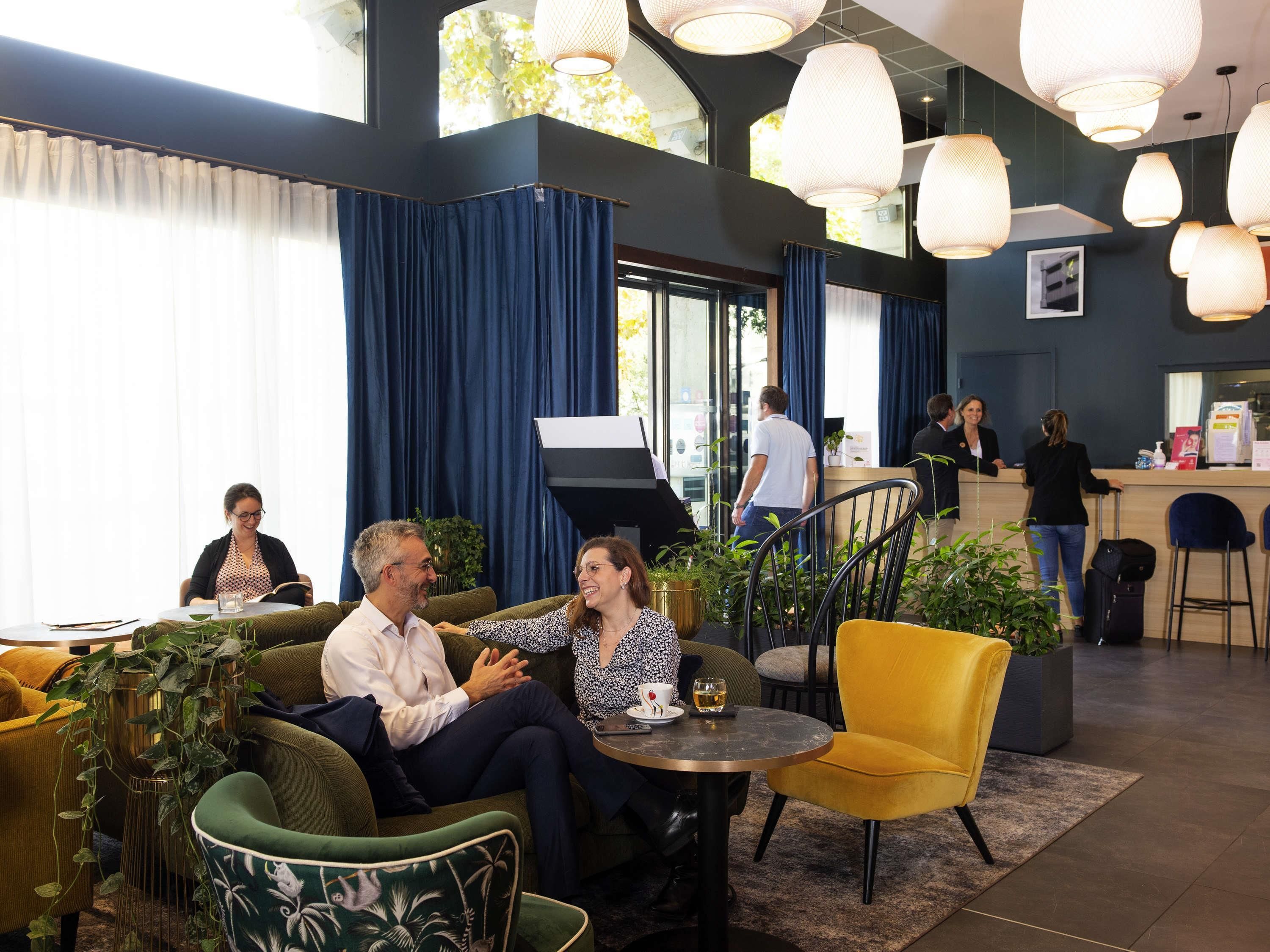 A modern hotel lobby with a seating area, a reception desk, and large windows.