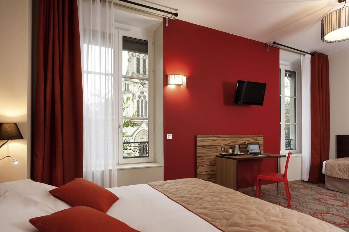 A hotel room with a large bed, a desk with a chair, a television, and a window with curtains.