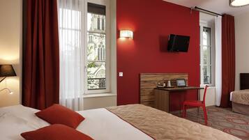Habitación de hotel con una cama grande, un escritorio con silla, televisor y ventana con cortinas.