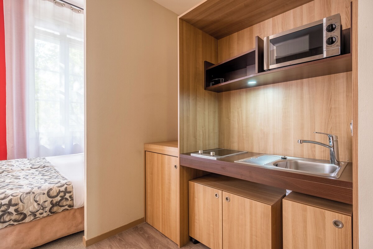 A compact kitchenette with a microwave, sink, and wooden cabinets.
