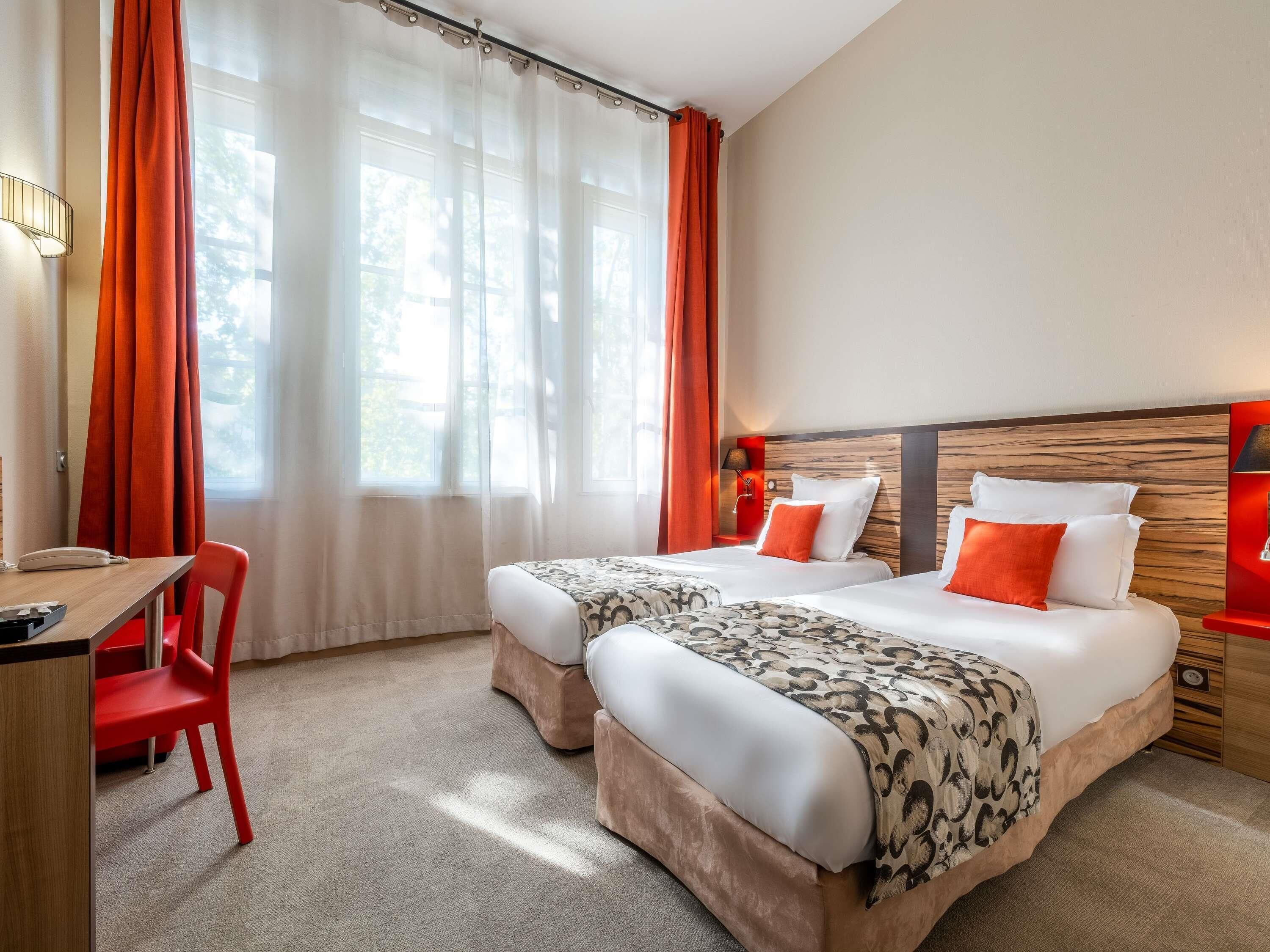 A hotel room with two beds, a desk, a chair, and a window with curtains.
