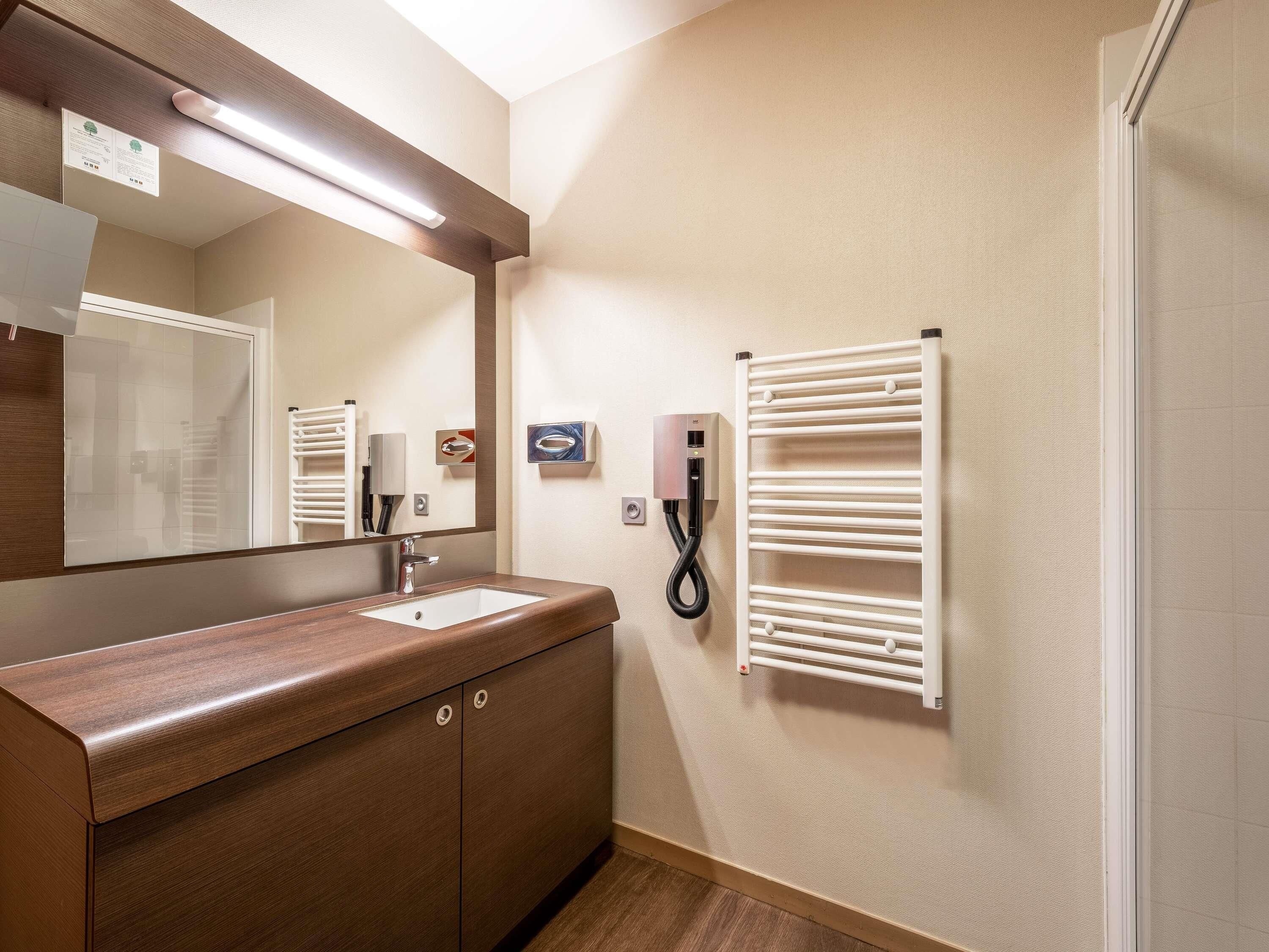Une salle de bain avec un meuble-lavabo en bois, un miroir, un porte-serviettes et un sèche-mains.