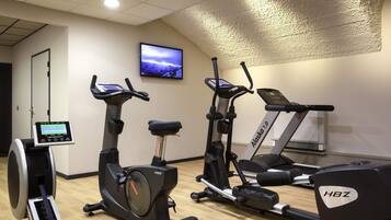 A gym with stationary bikes, treadmills, and a wall-mounted TV.