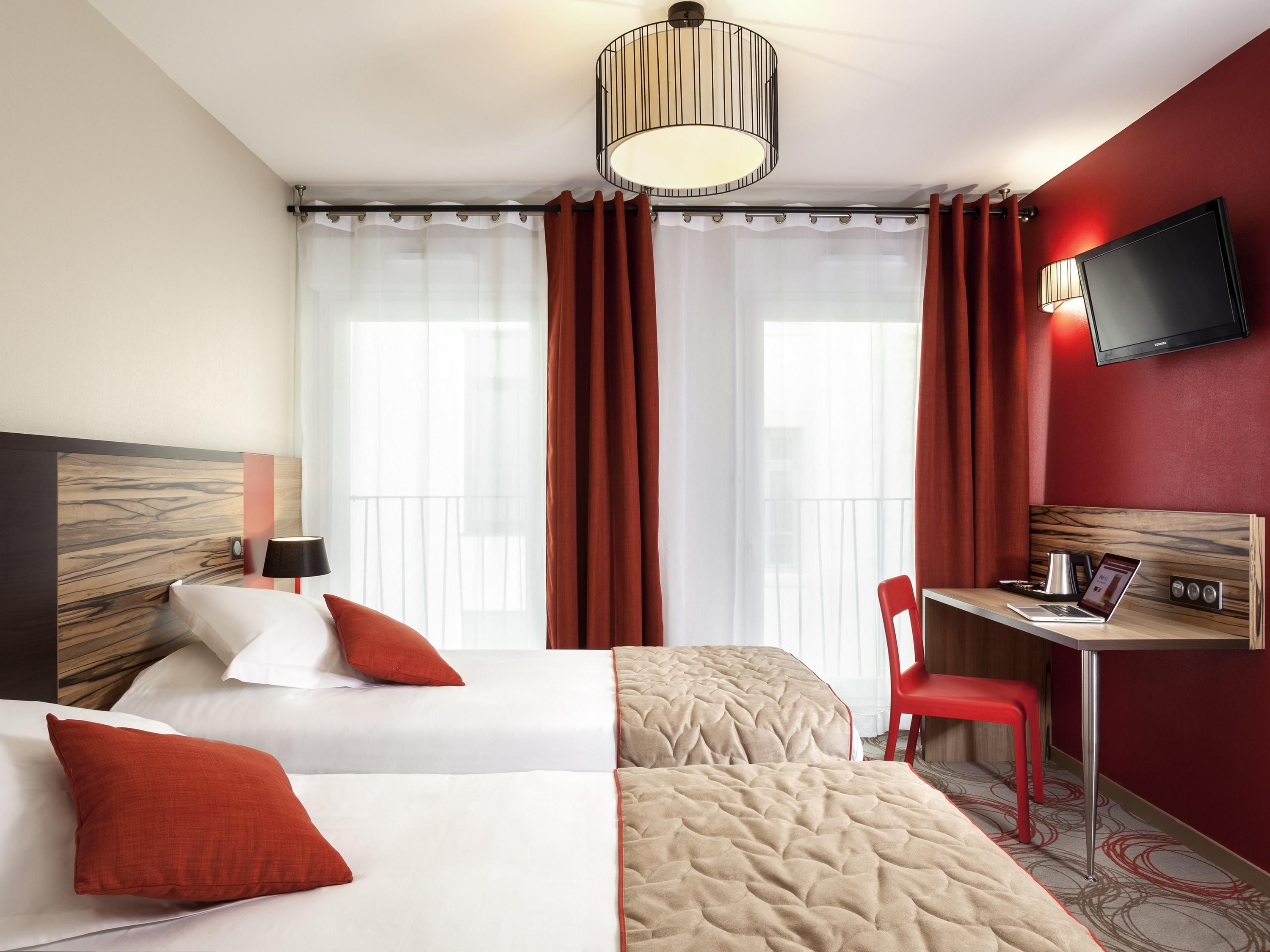 A hotel room with a bed, a desk with a laptop, a TV, and a chair.