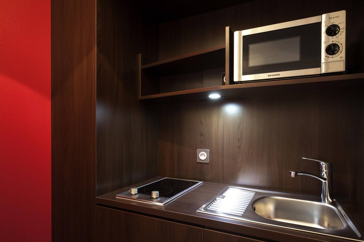 A compact kitchenette with a microwave, sink, and stovetop.