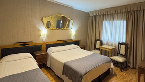 Habitació d'hotel amb dos llits, un terra de fusta, un mirall, una taula petita i una cadira.