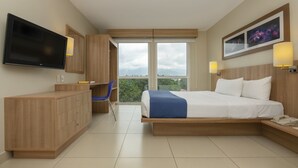 A modern hotel room with a large bed, a desk, a TV, and a view of the outdoors. - City Express by Marriott San Jose Costa Rica (Ulloa)