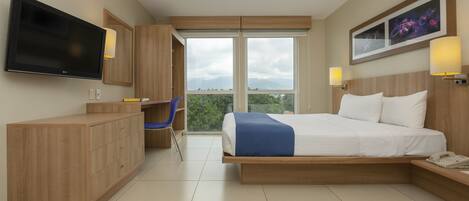 A modern hotel room with a large bed, a desk, a TV, and a view of the outdoors.