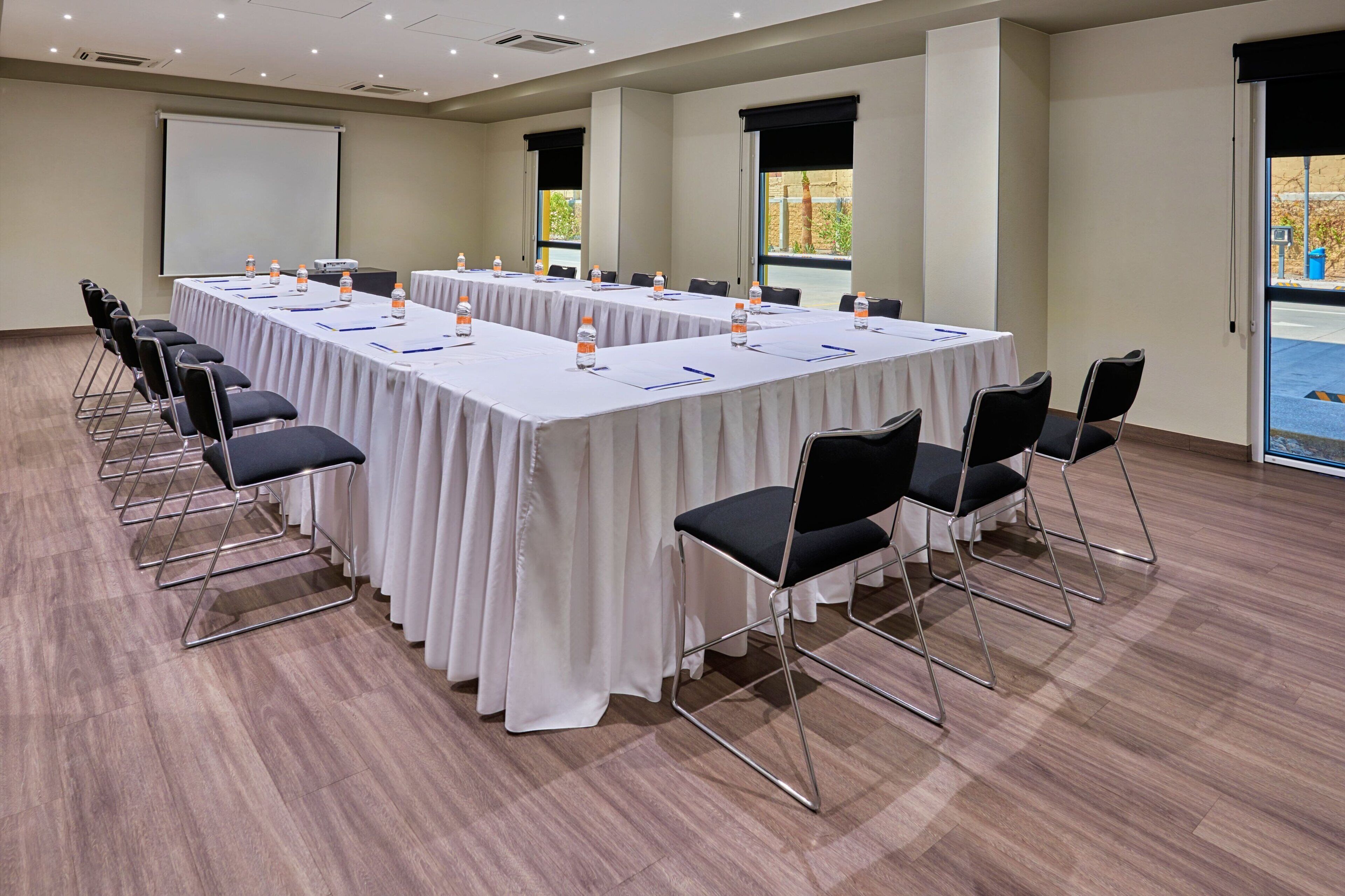 A conference room with a long table, chairs, and a projector screen.