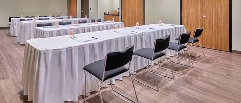 Un salón de conferencias con mesas largas, sillas y botellas de agua.