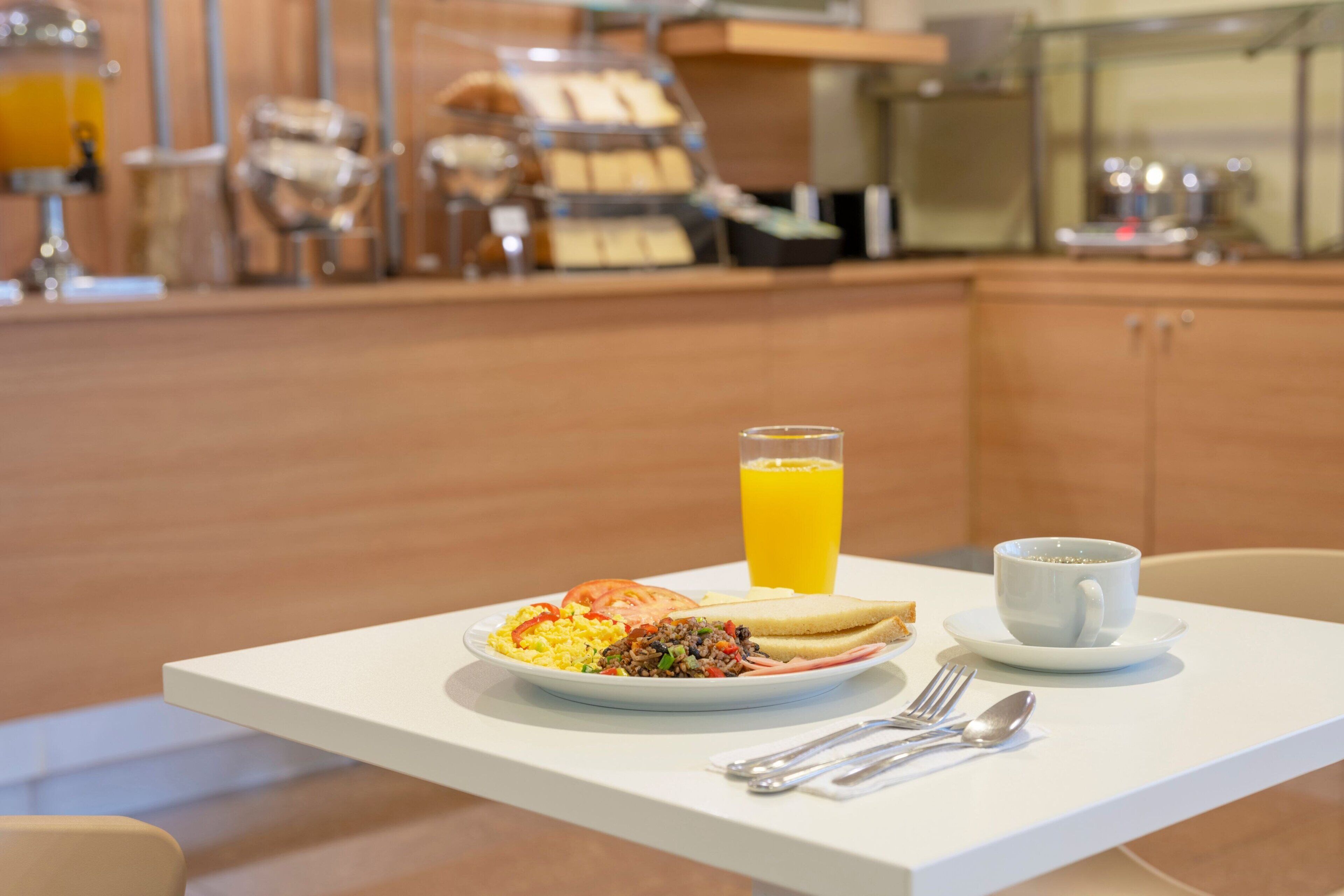 Mesa de café da manhã com um prato de comida, um copo de suco de laranja e uma xícara de café.