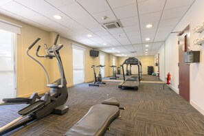Ein Fitnessbereich im Hotel mit Laufbändern, Crosstrainern und einer Bank.