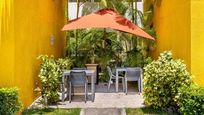 An outdoor seating area with a table and chairs, a red umbrella, and lush greenery. - City Express by Marriott San Jose Costa Rica (Ulloa)