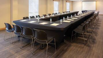 A conference room with a long table, chairs, water bottles, and a projector screen.
