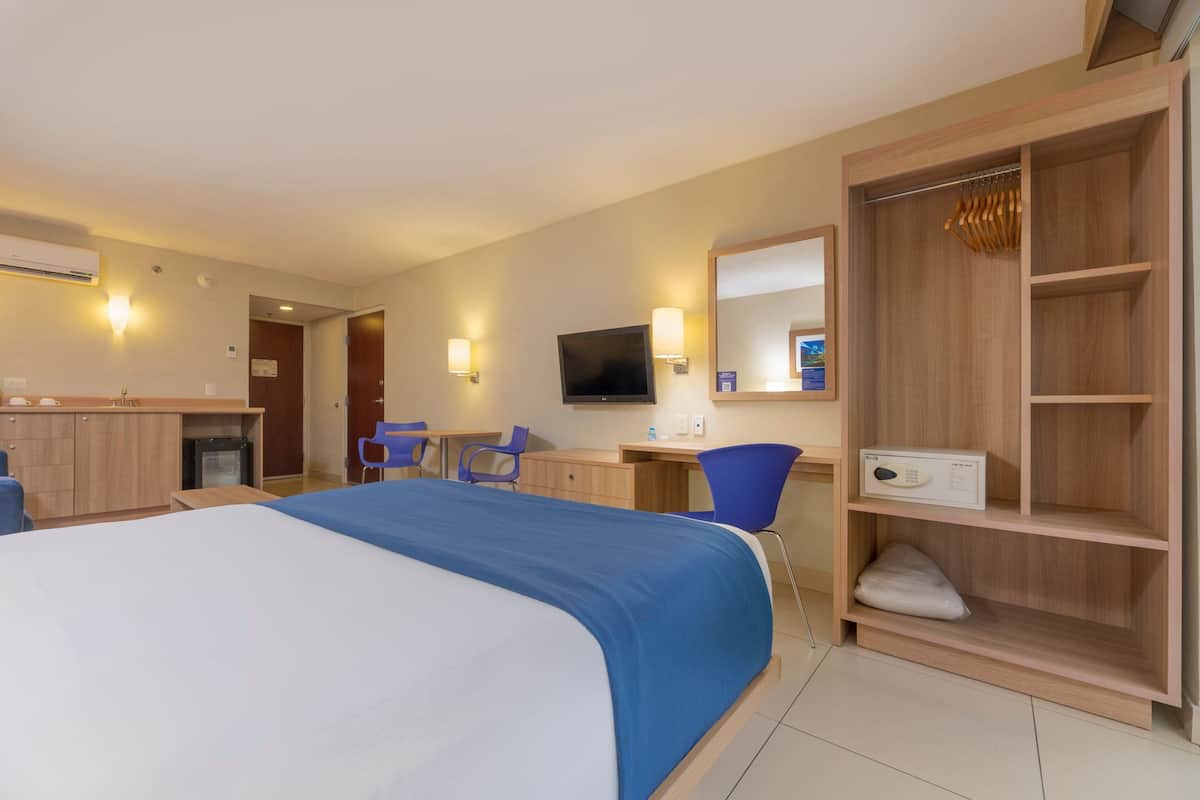 Une chambre d’hôtel équipée d’un lit, d’un bureau, d’une chaise, d’une armoire, d’une télévision et d’un miroir.