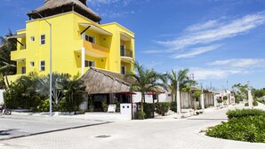 A yellow building with a thatched roof, surrounded by greenery and palm trees.