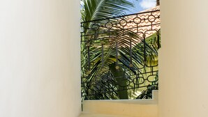 A narrow stairway leading to a balcony with a view of a palm tree and a building with a patterned facade.