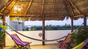 A thatched-roof outdoor area with two wooden chairs and a hammock.