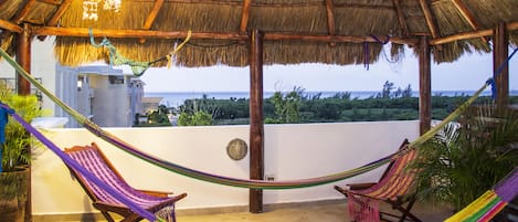 A thatched-roof outdoor area with two wooden chairs and a hammock.