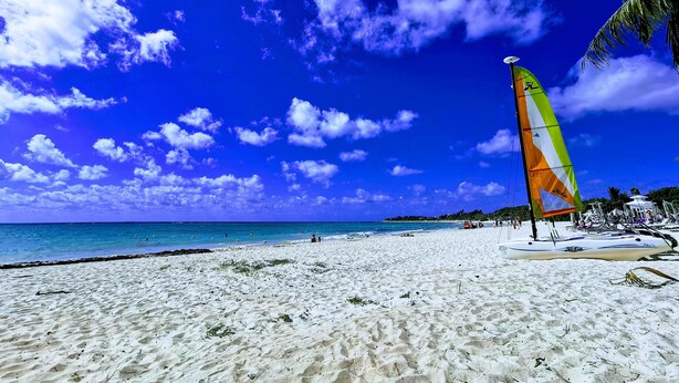 A beach with a sailboat, clear blue sky, and ocean.