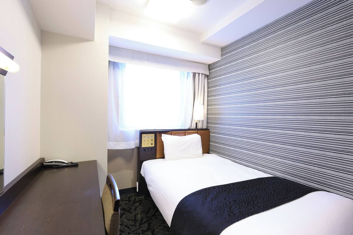 A hotel room with a bed, a desk, and a window with curtains.