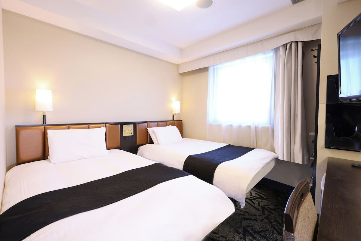 A hotel room with two beds, a TV, and a window with curtains.
