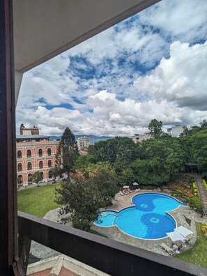 A view of a swimming pool surrounded by greenery, a red building, and a clear sky. - Hotel Yak & Yeti (Kathmandu)