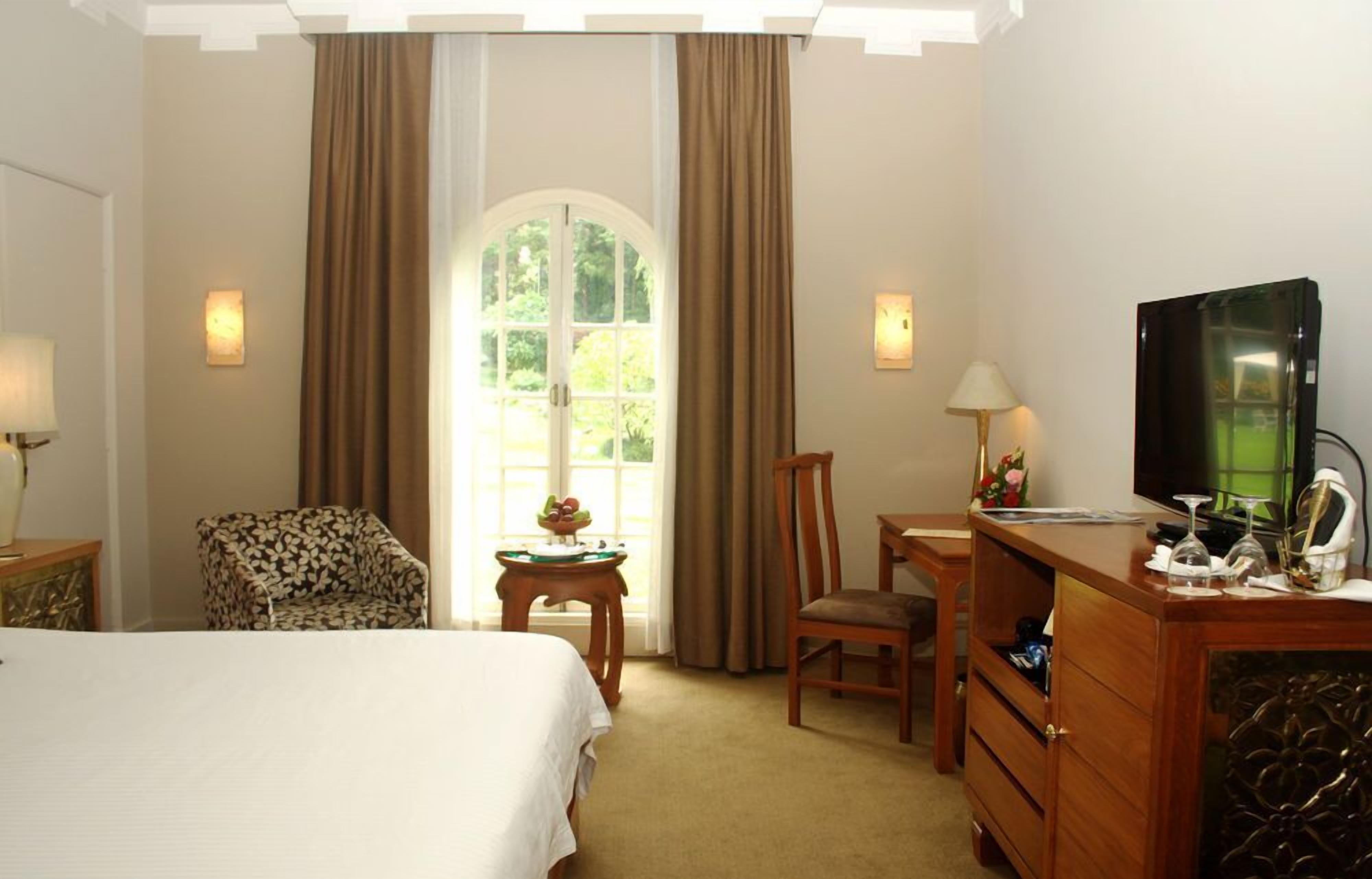 Een hotelkamer met een bed, een bureau, een stoel, een televisietoestel en een raam met gordijnen.