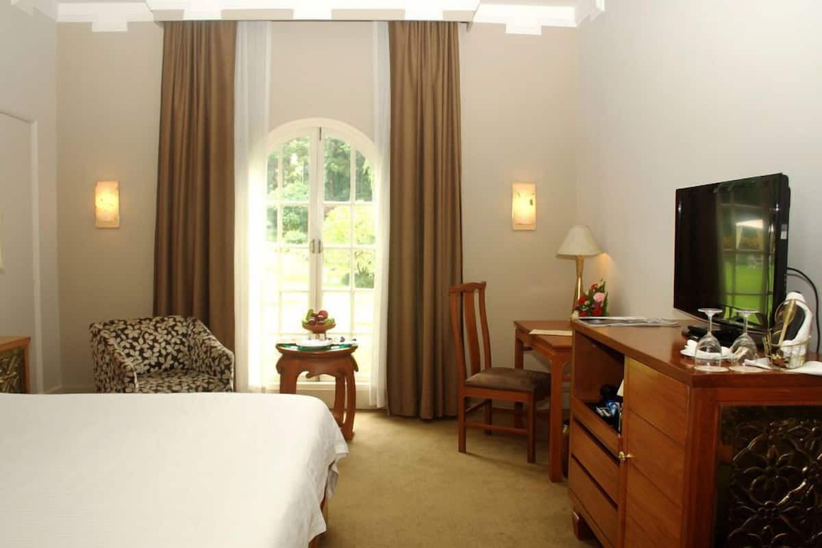 Ein Hotelzimmer mit Bett, Schreibtisch, Sessel, Fernseher und einem fensterbepflanzten Fenster.
