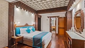 A hotel room with a wooden headboard, a large bed, a nightstand, a mirror, and a wooden floor.
