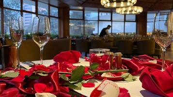 A dining table set with wine glasses, rose petals, and a rolled napkin with a ribbon.