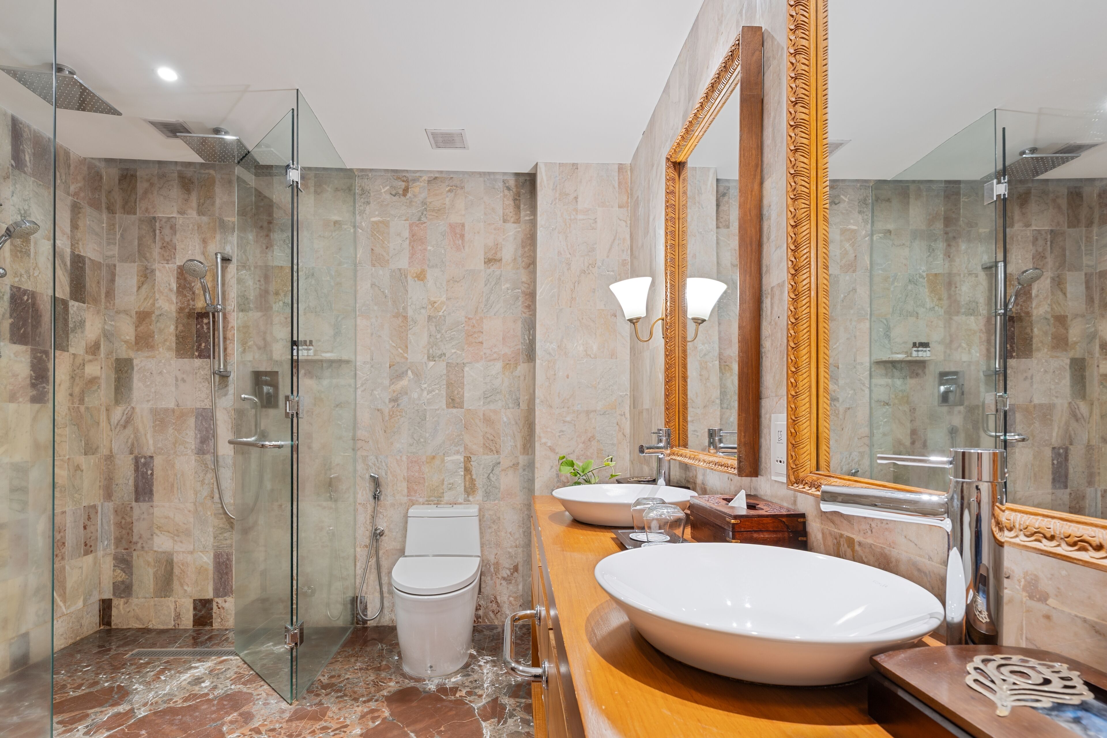 A modern bathroom with a glass-enclosed shower, a white toilet, a large oval sink, and a mirror with an ornate frame.