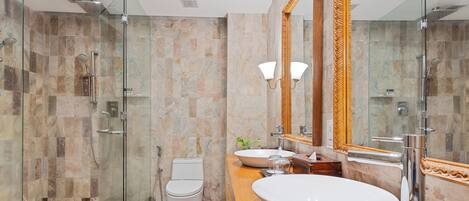 Un baño moderno con ducha envuelta en vidrio, inodoro blanco, un lavamanos ovalado grande y un espejo con marco decorativo.