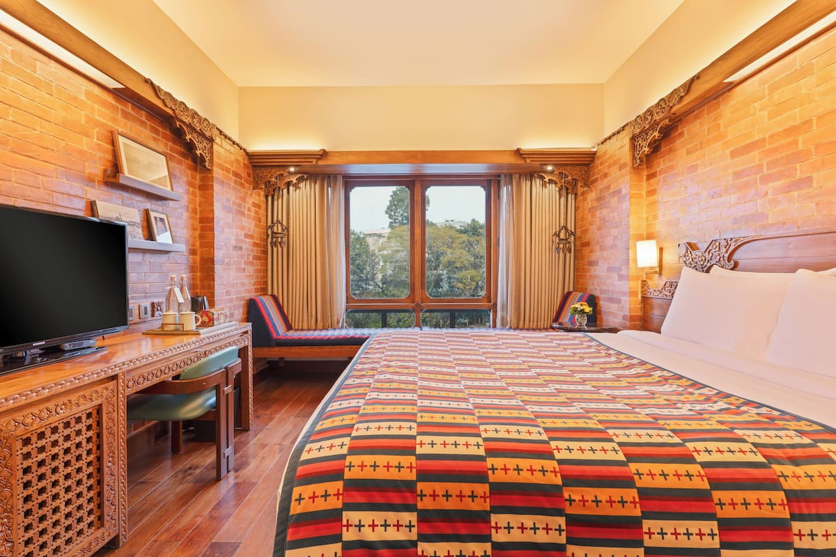 Ein Hotelzimmer mit einem großen Bett, einem Fernseher, einem Schreibtisch mit Stuhl und einem fenster mit Vorhängen.