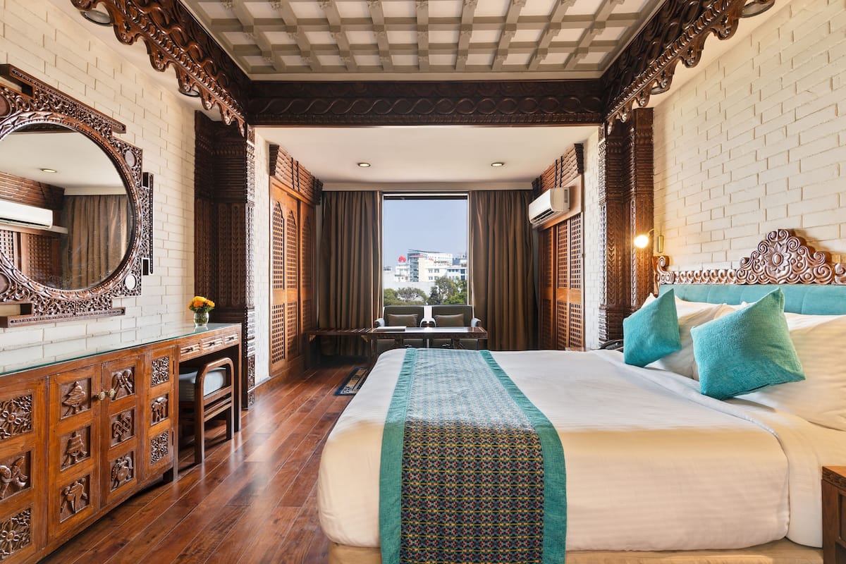 Ein Hotelzimmer mit einem großen Bett, einem Schreibtisch, einem Stuhl, einem Spiegel und Blick auf Gebäude.