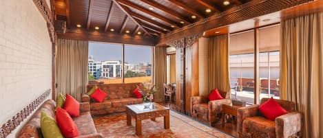 A spacious lounge with patterned sofas, a coffee table, and a large window offering a city view.