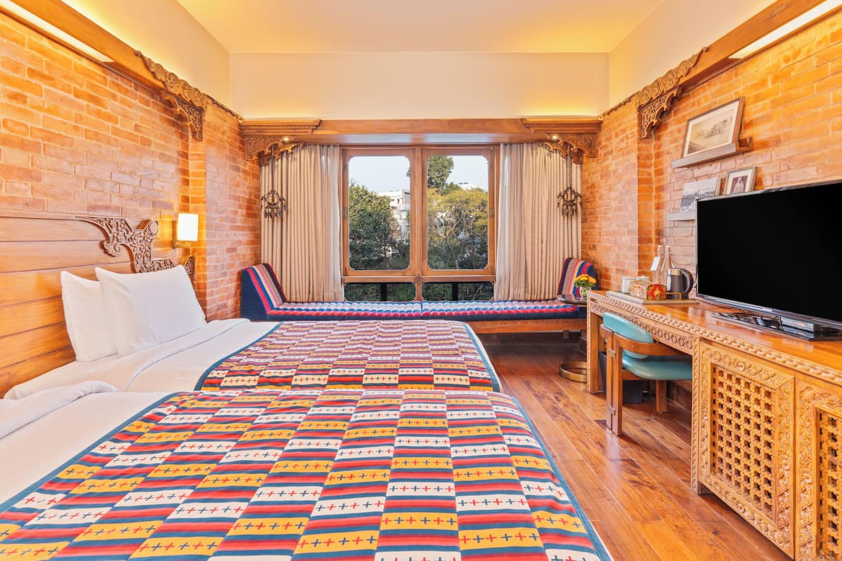 Ein Hotelzimmer mit einem großen Bett, einem Holztisch, einem Fernseher und einem Fenster mit Vorhängen.