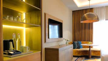 A hotel room with a wooden cabinet, a television mounted on the wall, a sofa, a small table, and a patterned rug.