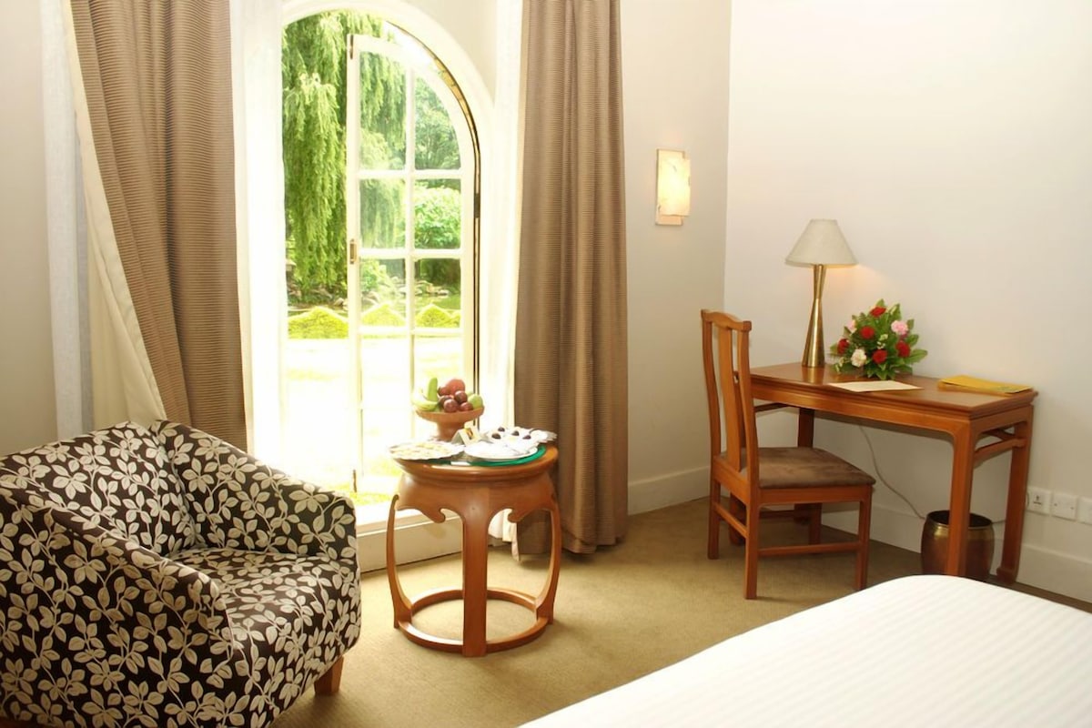 A hotel room with a bed, a desk with a chair, a small table with a lamp, and a sofa.