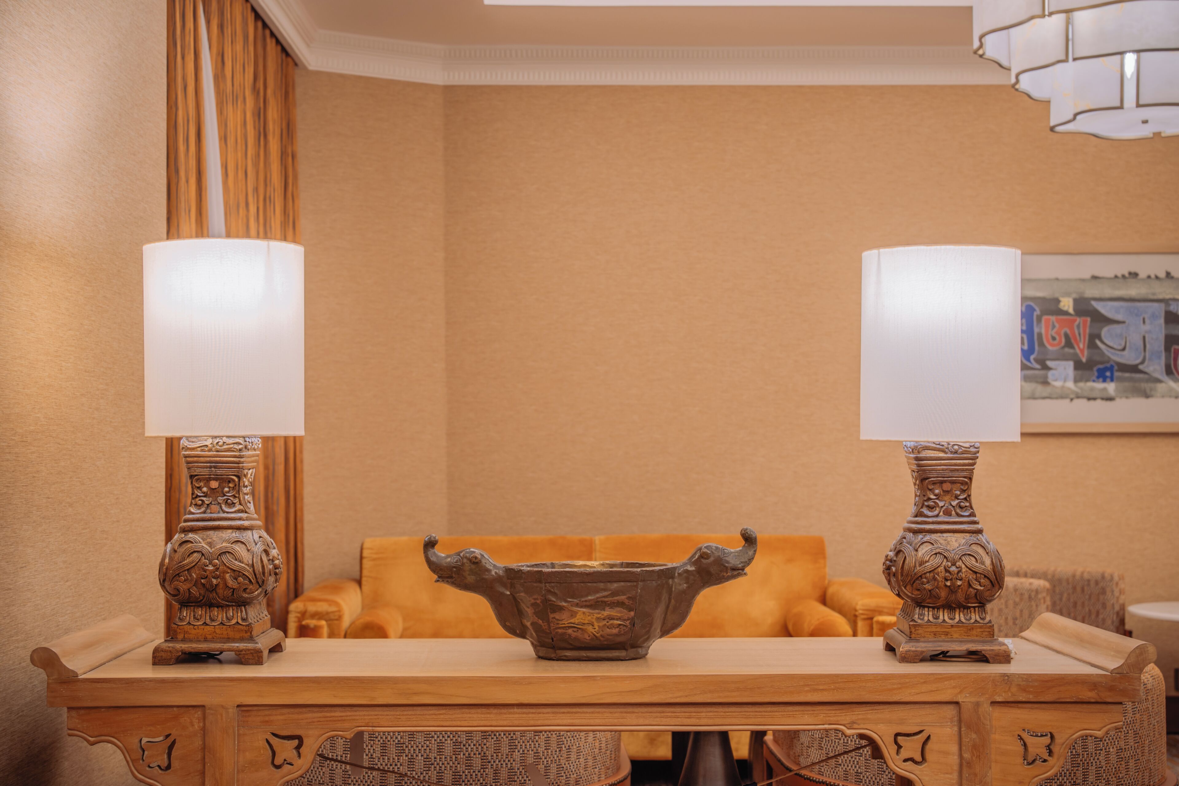 A wooden table with two ornate lamps, a decorative bowl, and a cushioned sofa in a warmly lit room.