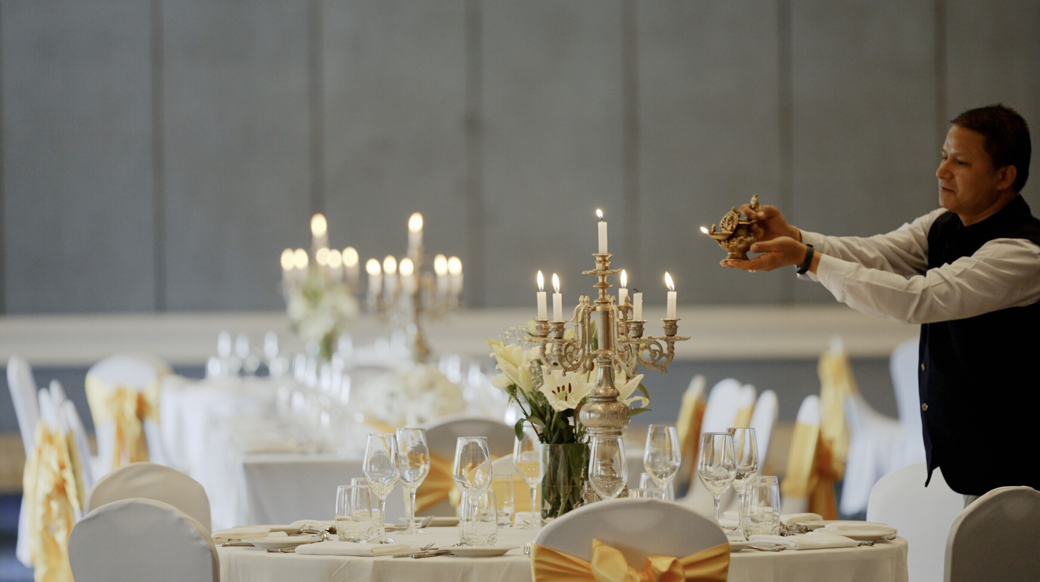 Un ambiente formal para cenar, con mesas dispuestas para una comida, centros de mesa con velas y un camarero sirviendo.