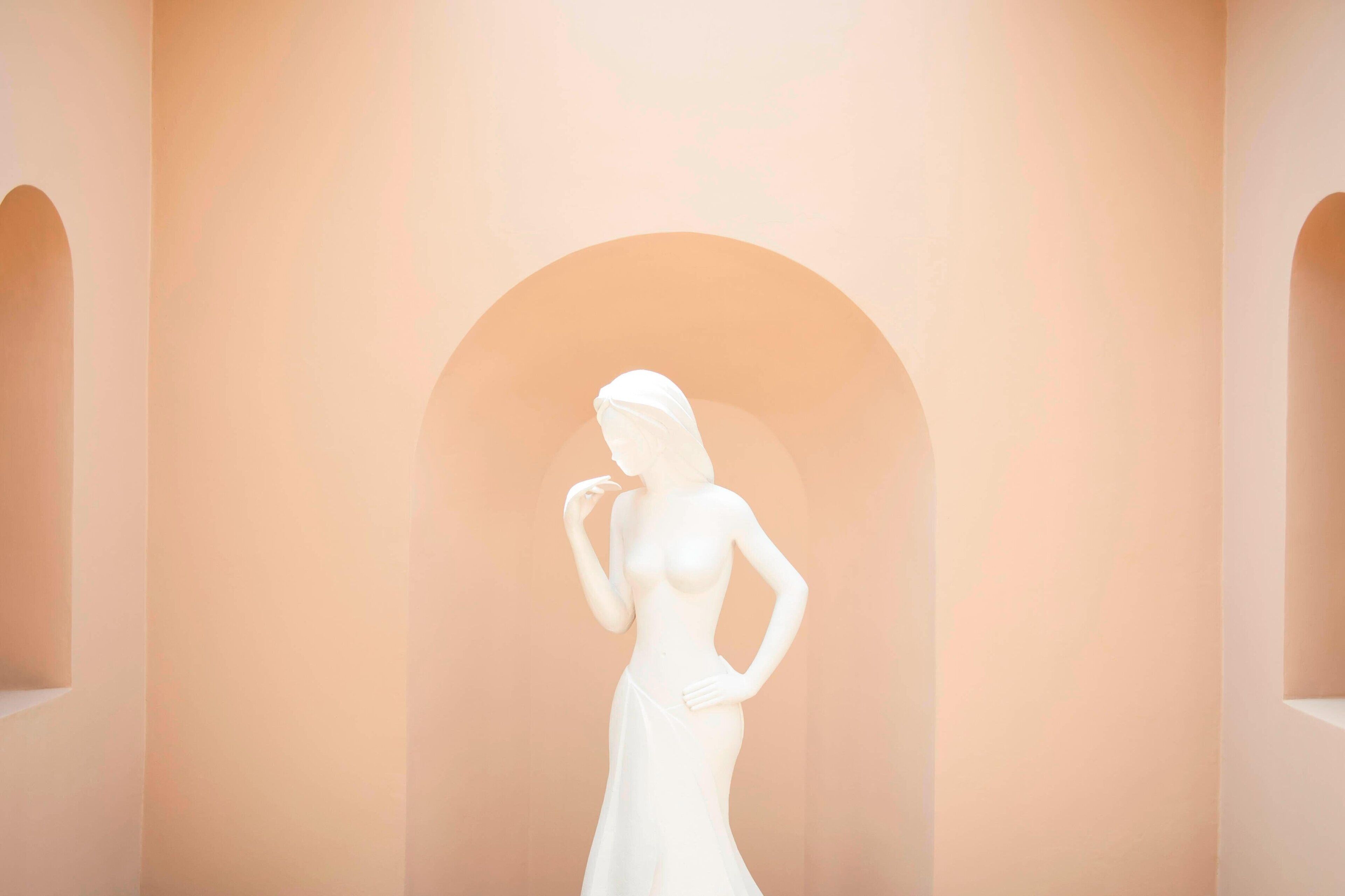 A white statue of a woman in a dress standing in an arched doorway.