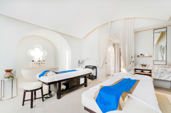 A modern spa room with a massage table, a small sitting area, and a vanity with a mirror. - Vana Belle, a Luxury Collection Resort, Koh Samui (Koh Samui)