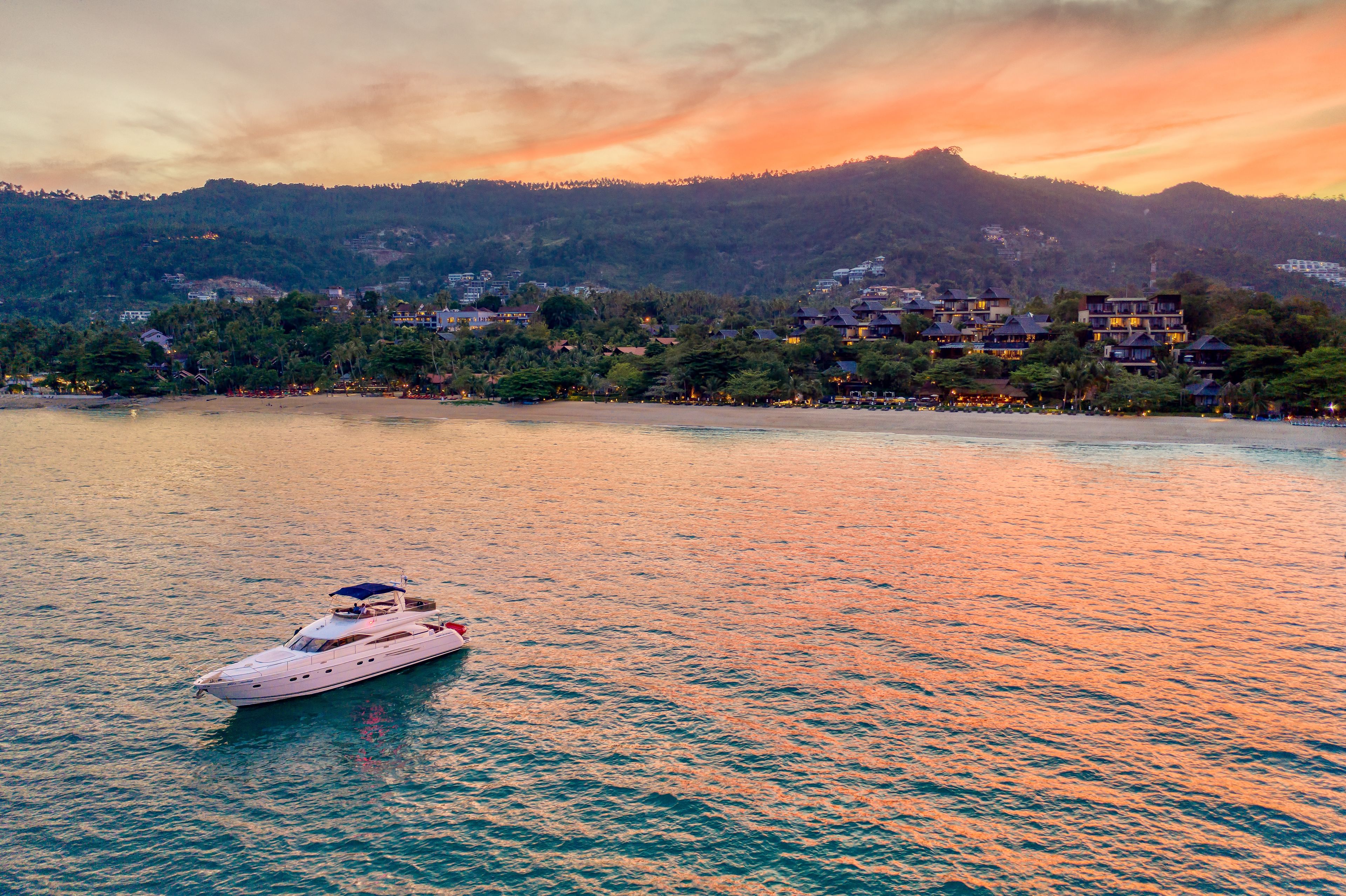 A yacht on calm waters with a backdrop of a mountainous landscape and a sunset.
