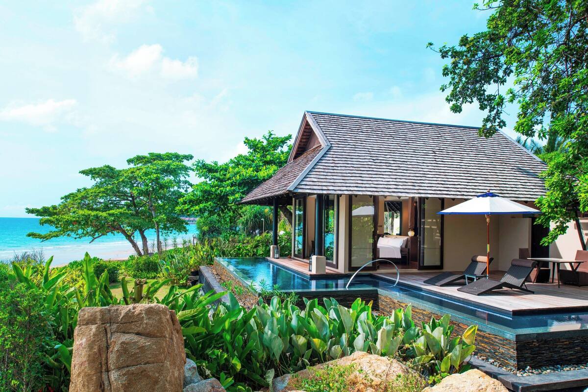 A modern villa with a pool, overlooking the ocean, surrounded by lush greenery.