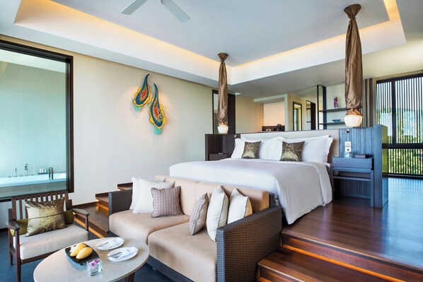 A modern hotel room with a large bed, a sofa, a dining table, and a balcony with a view.