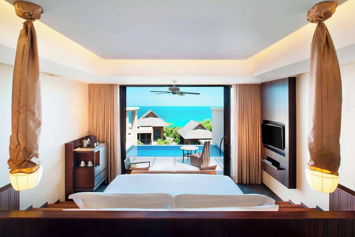 A hotel room with a bed, a TV, a desk, and a view of the ocean.