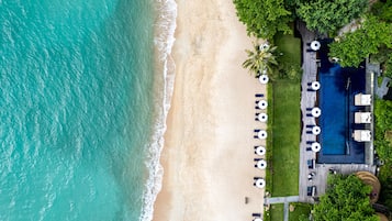 An aerial view of a beachside resort with a swimming pool, lounge chairs, and a well-maintained lawn.