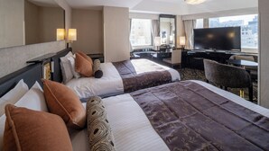 Een hotelkamer met twee bedden, een bureau, een televisie en een groot raam met uitzicht op de stad.